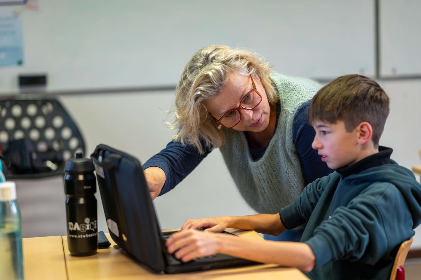 Een leerkracht helpt een leerling aan zijn laptop